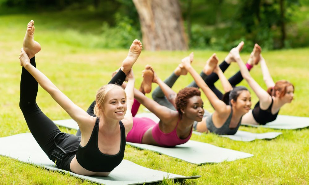 Happy diverse girls doing bow yoga pose on outdoor yoga practice in nature